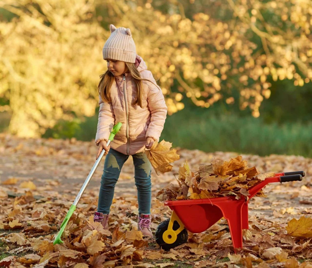 A young child rakes leaves in the grass.